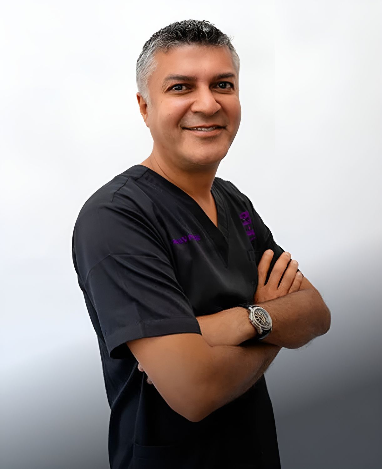 Smiling professional in medical scrubs with arms crossed.