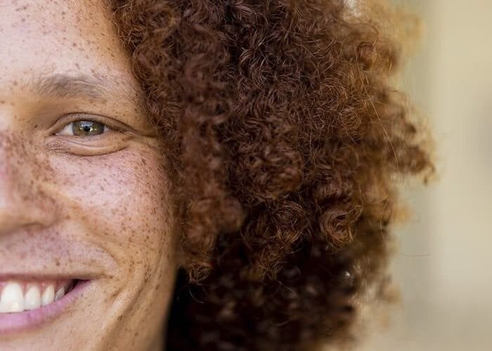 Smiling person with curly hair against blue background.