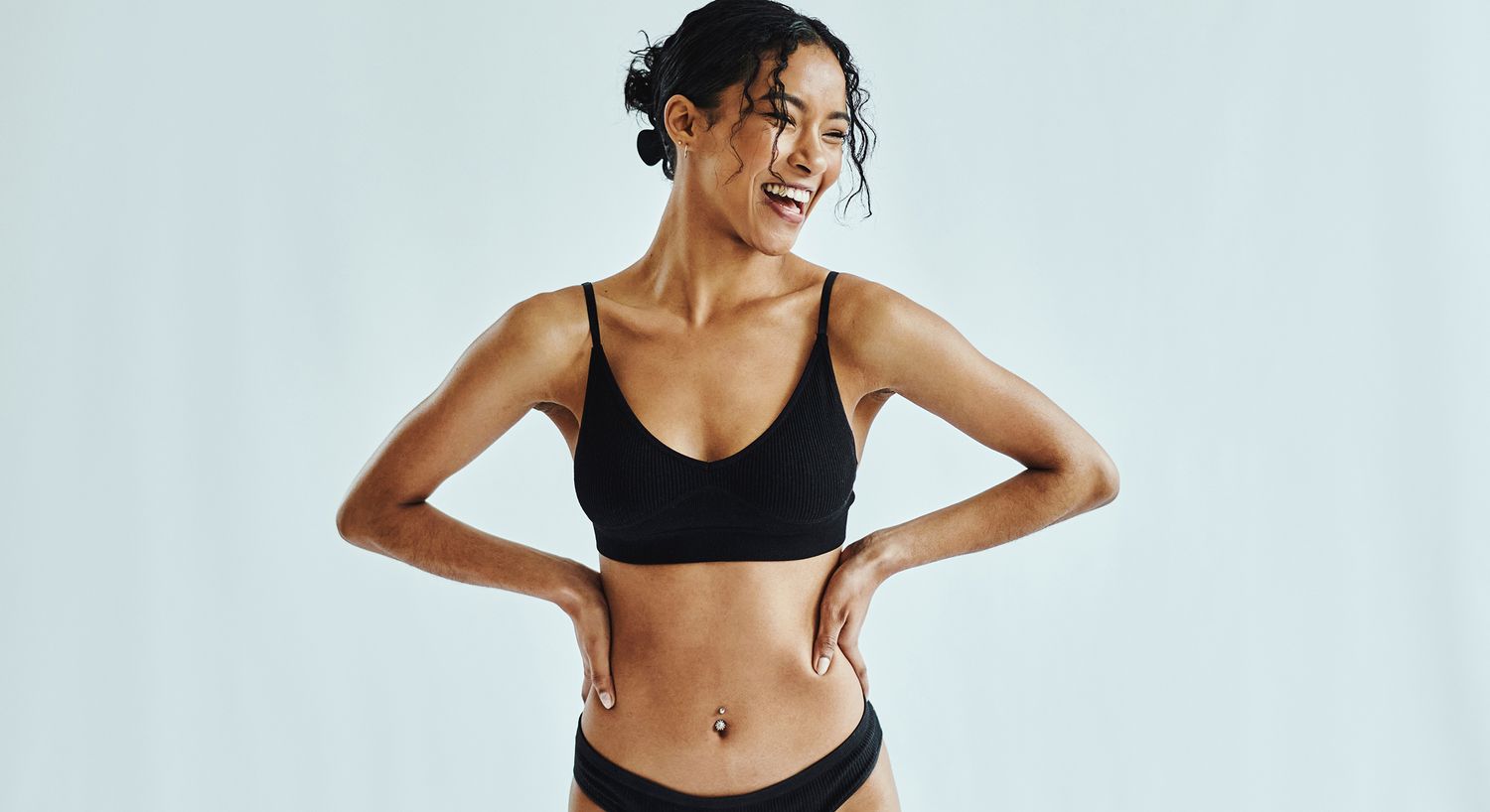 Woman smiling in black undergarments with a flat tummy.