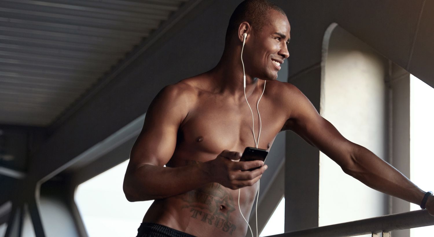 Shirtless man listening to music on balcony.