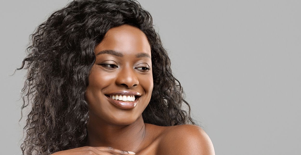 Smiling woman with curly hair against gray background.
